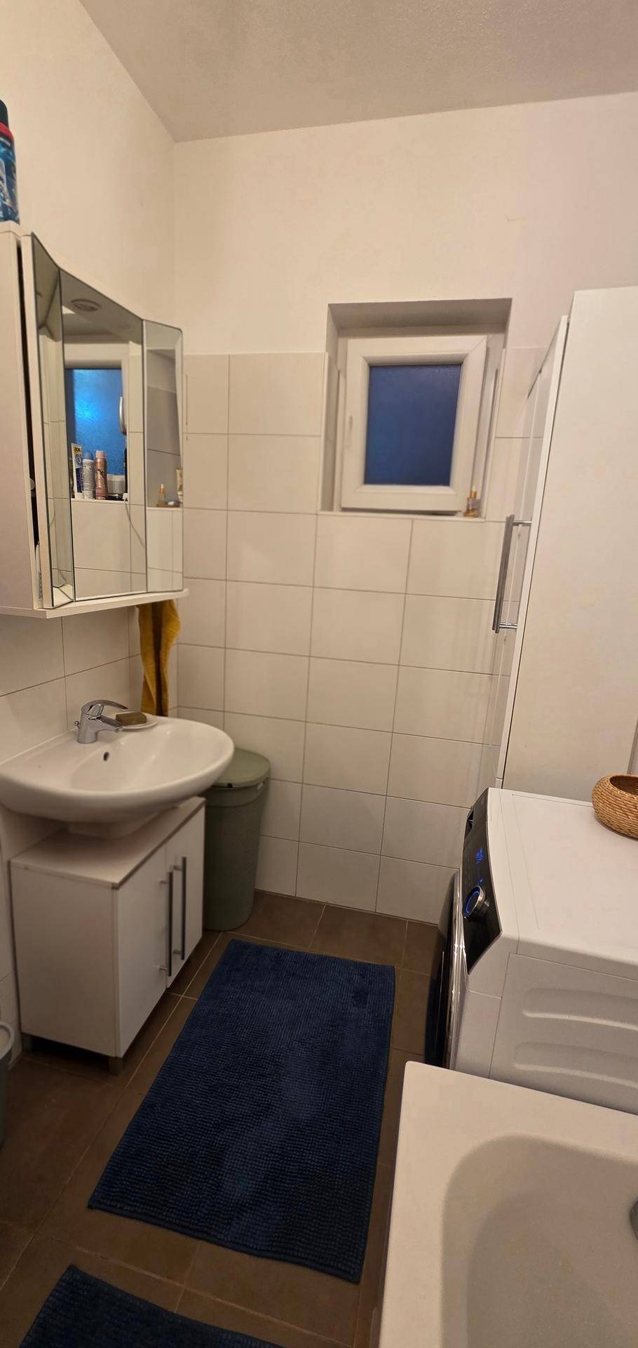 Helles Badezimmer mit Waschbecken, Spiegelschrank, Fenster und Waschmaschine.