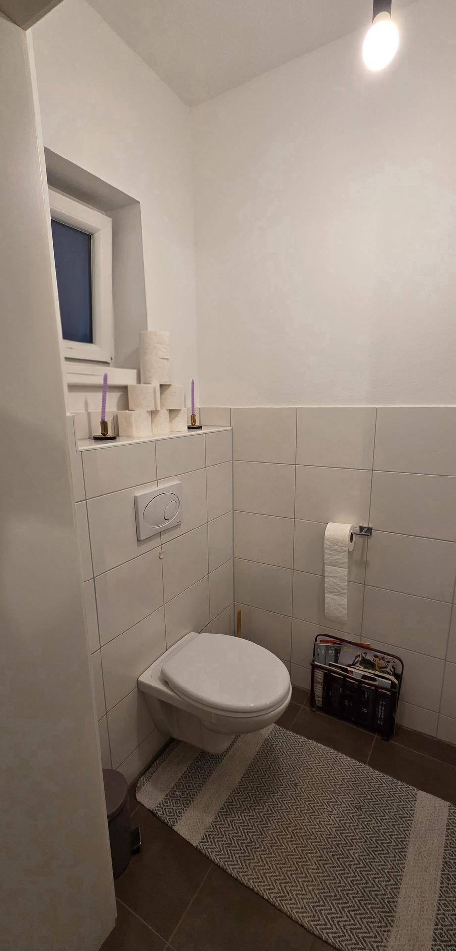 Helles Gäste-WC mit Fenster, Wand-WC und halbhohen Fliesen.