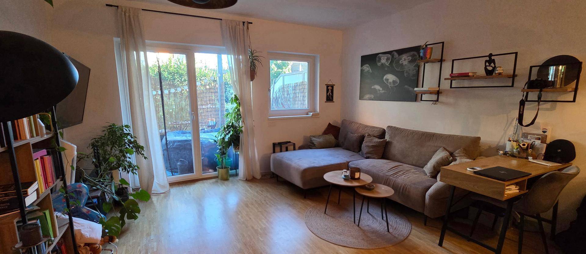 Helles Wohnzimmer mit beigem Ecksofa, vielen Pflanzen und Zugang zum Garten.