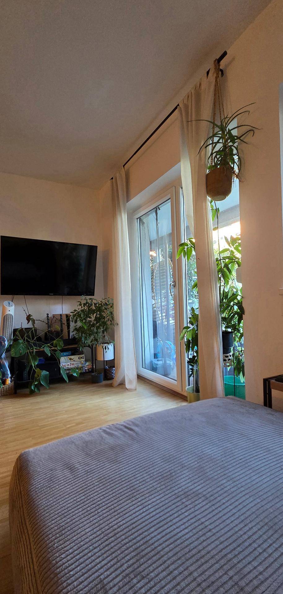 Schlafzimmer mit Bett, Fernseher und großem Fenster mit Blick ins Grüne.