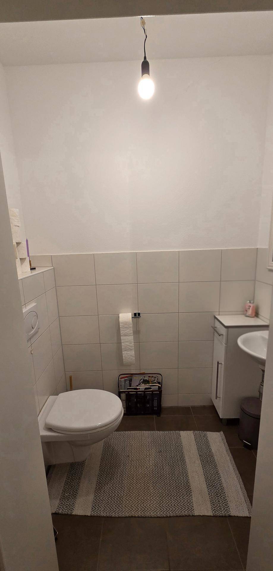 Modernes Gäste-WC mit Wand-WC, kleinem Waschbecken und hellen Fliesen.
