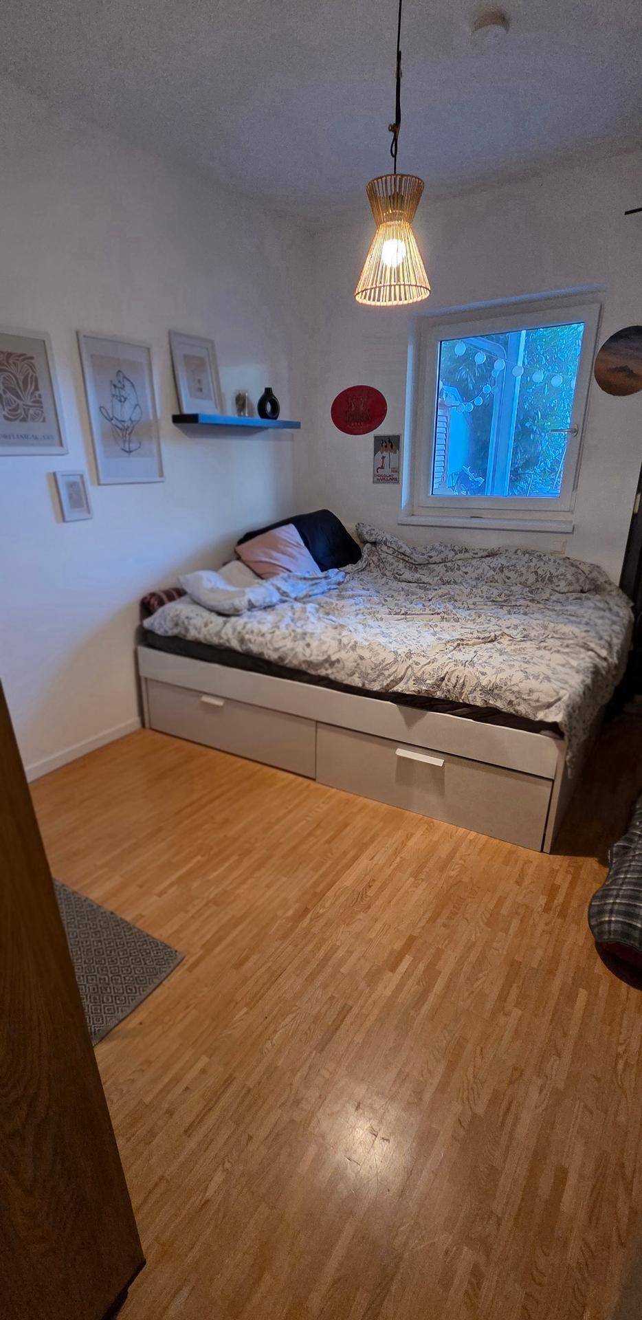Schlafzimmer mit Bett mit Stauraum, Holzboden und Fenster.