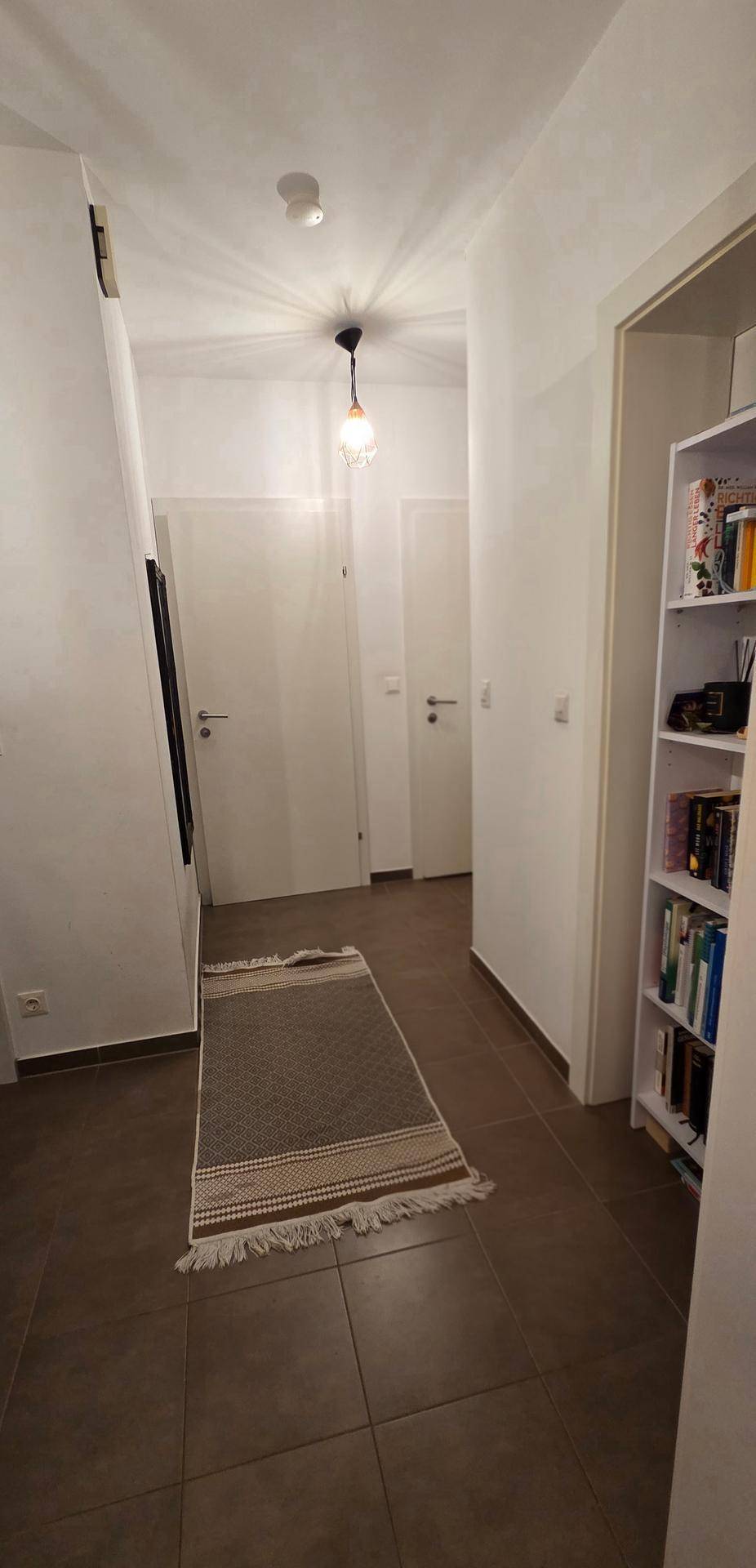 Heller Flur mit Fliesenboden, Bücherregal und Zugang zu verschiedenen Räumen.
