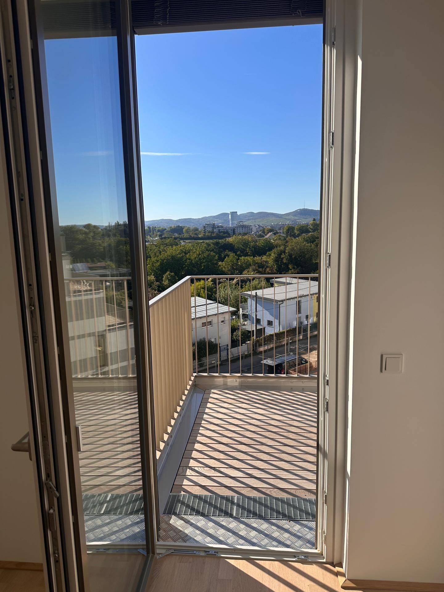 Heller Innenraum mit Zugang zum Balkon, der einen weiten Blick über die Stadt und grüne Umgebung bietet.