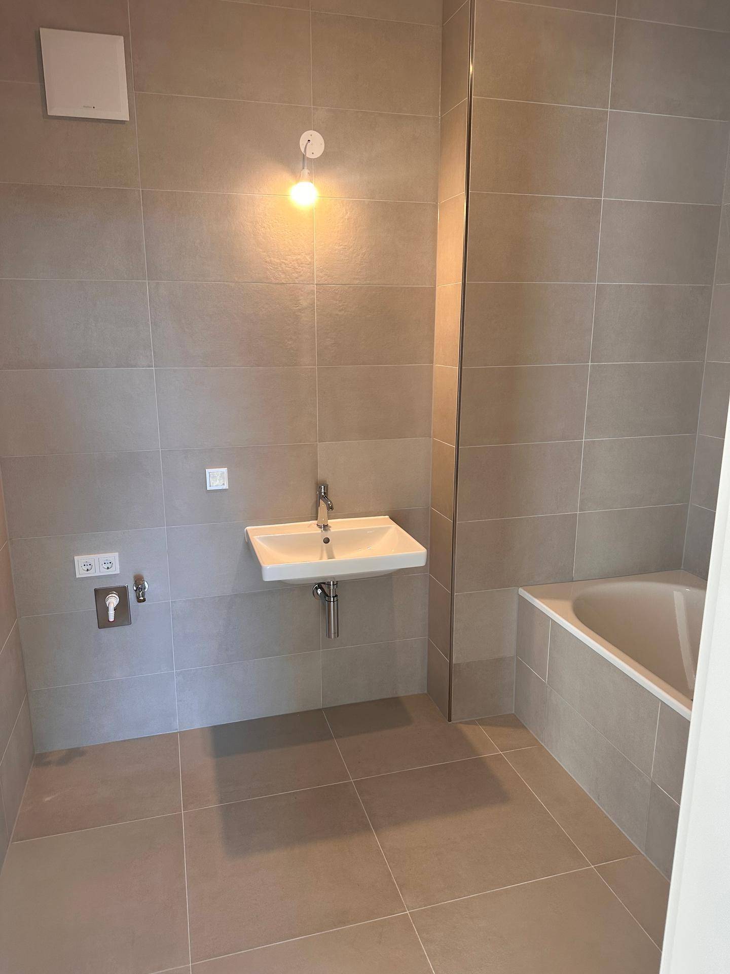 Modernes Badezimmer mit Badewanne, Einzelwaschbecken und hellgrauen Fliesen an Wänden und Boden.
