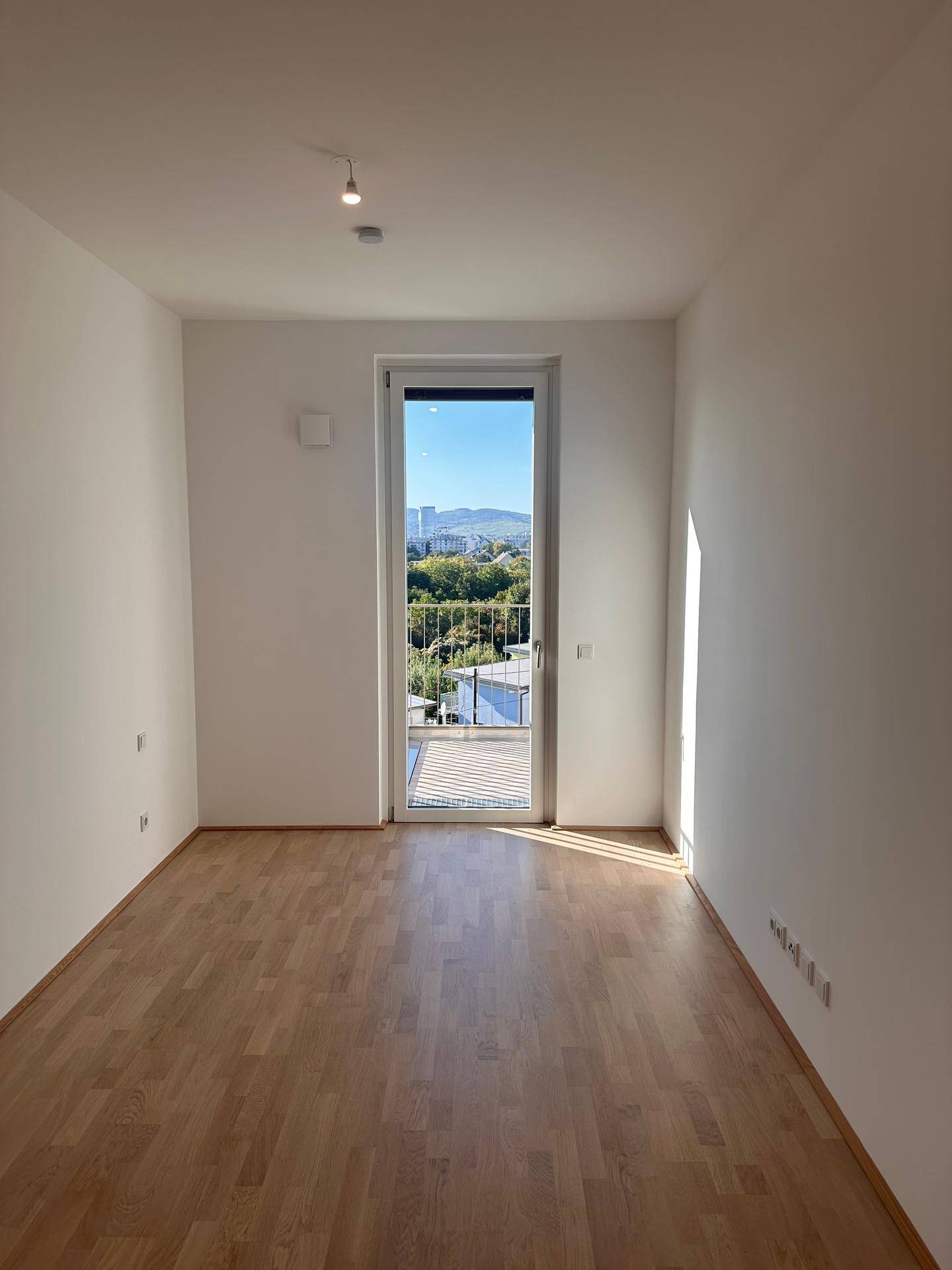 Heller Raum mit Parkettboden und Balkonzugang, bietet viel natürliches Licht und eine schöne Aussicht.