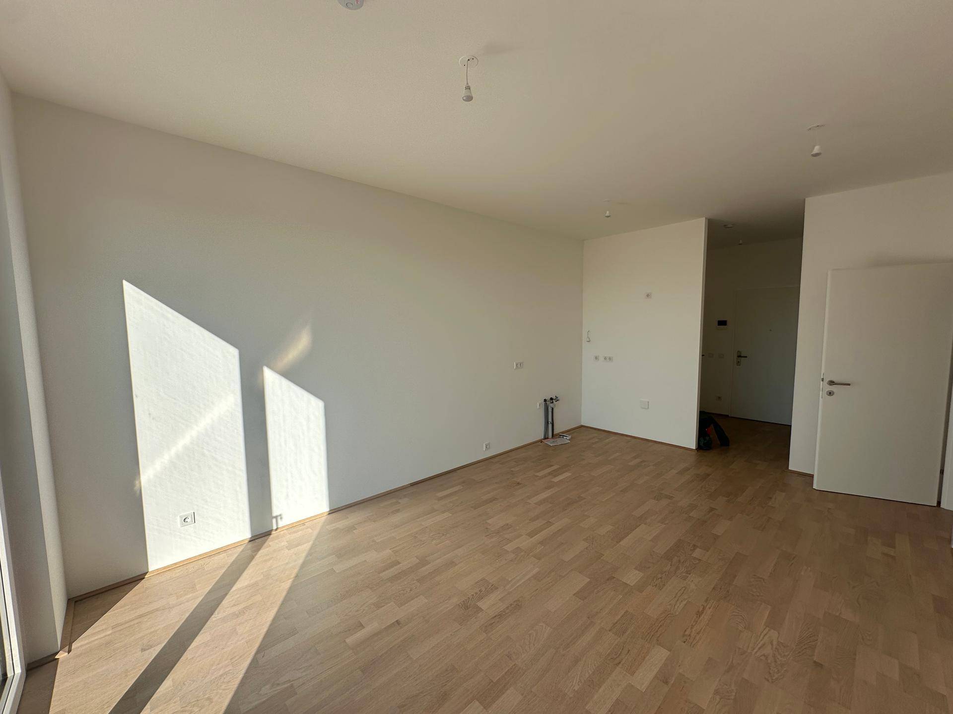 Geräumiger, leerer Küchenbereich mit vorbereiteten Anschlüssen und hellem Parkettboden.