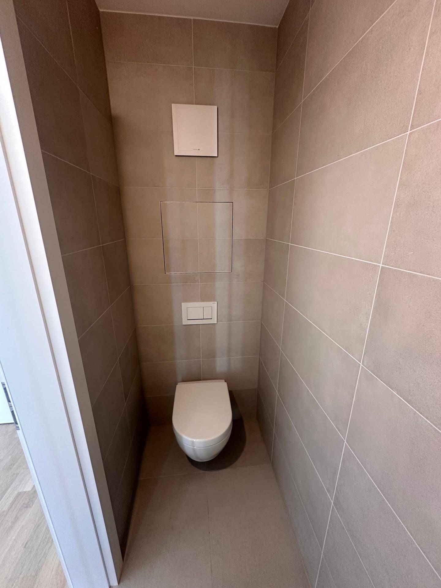 Modernes Gäste-WC mit wandhängender Toilette und hellgrauen Fliesen an Wänden und Boden.