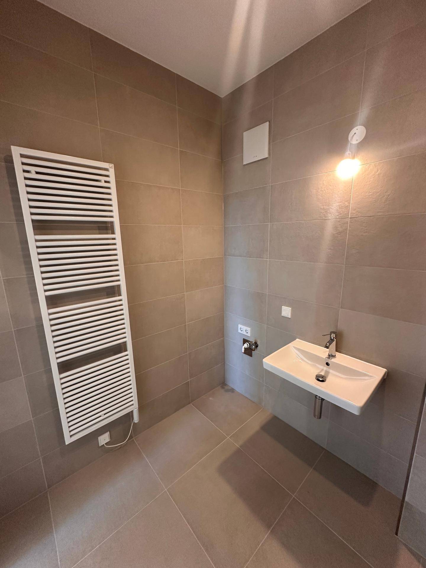 Badezimmer mit Einzelwaschbecken, beheiztem Handtuchhalter und modernen hellgrauen Fliesen.