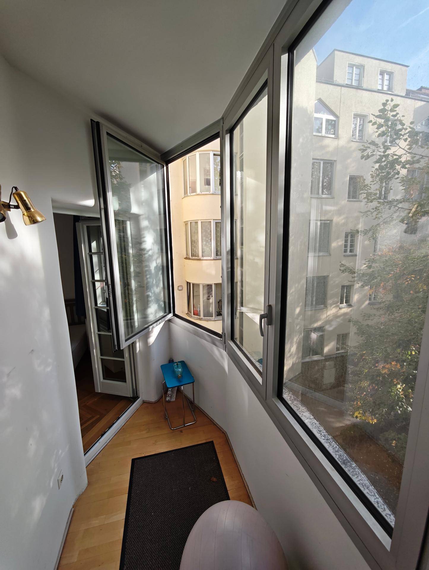 Helle Loggia mit Blick auf die umliegenden Gebäude und Bäume, mit Holzboden.