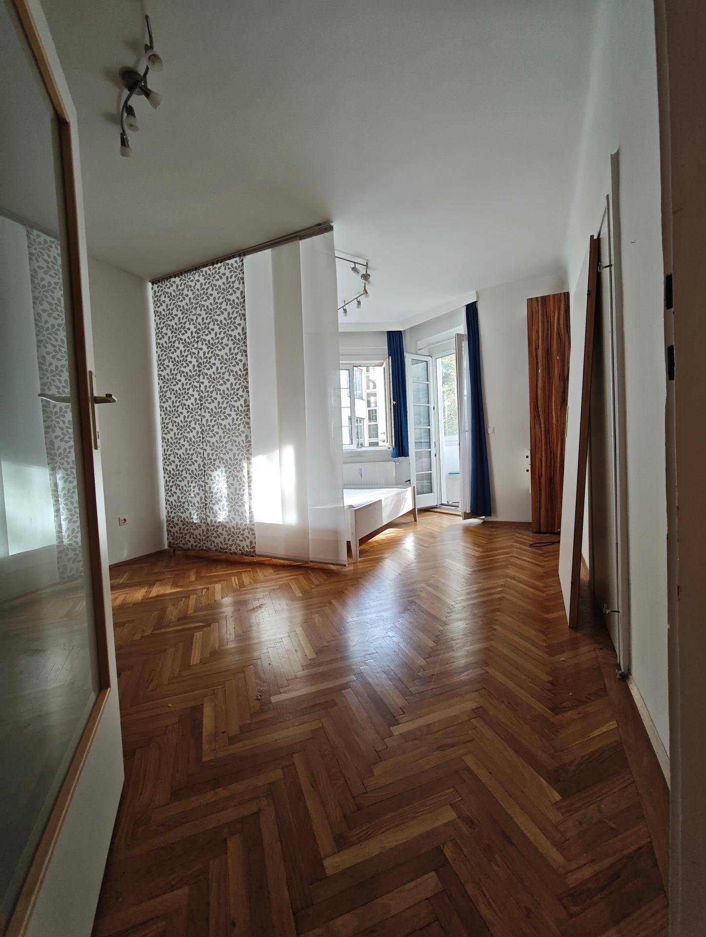 Heller Wohnraum mit elegantem Fischgrätparkett und Zugang zu einem Balkon.