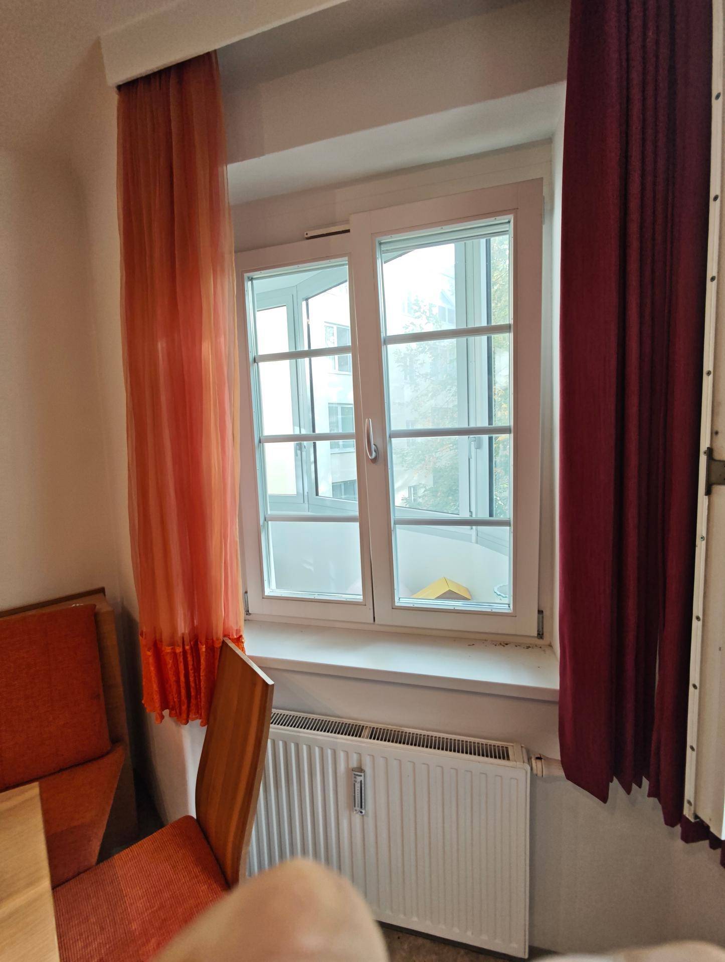 Fenster im Essbereich der Küche mit Vorhängen und Heizkörper, bietet Tageslicht.