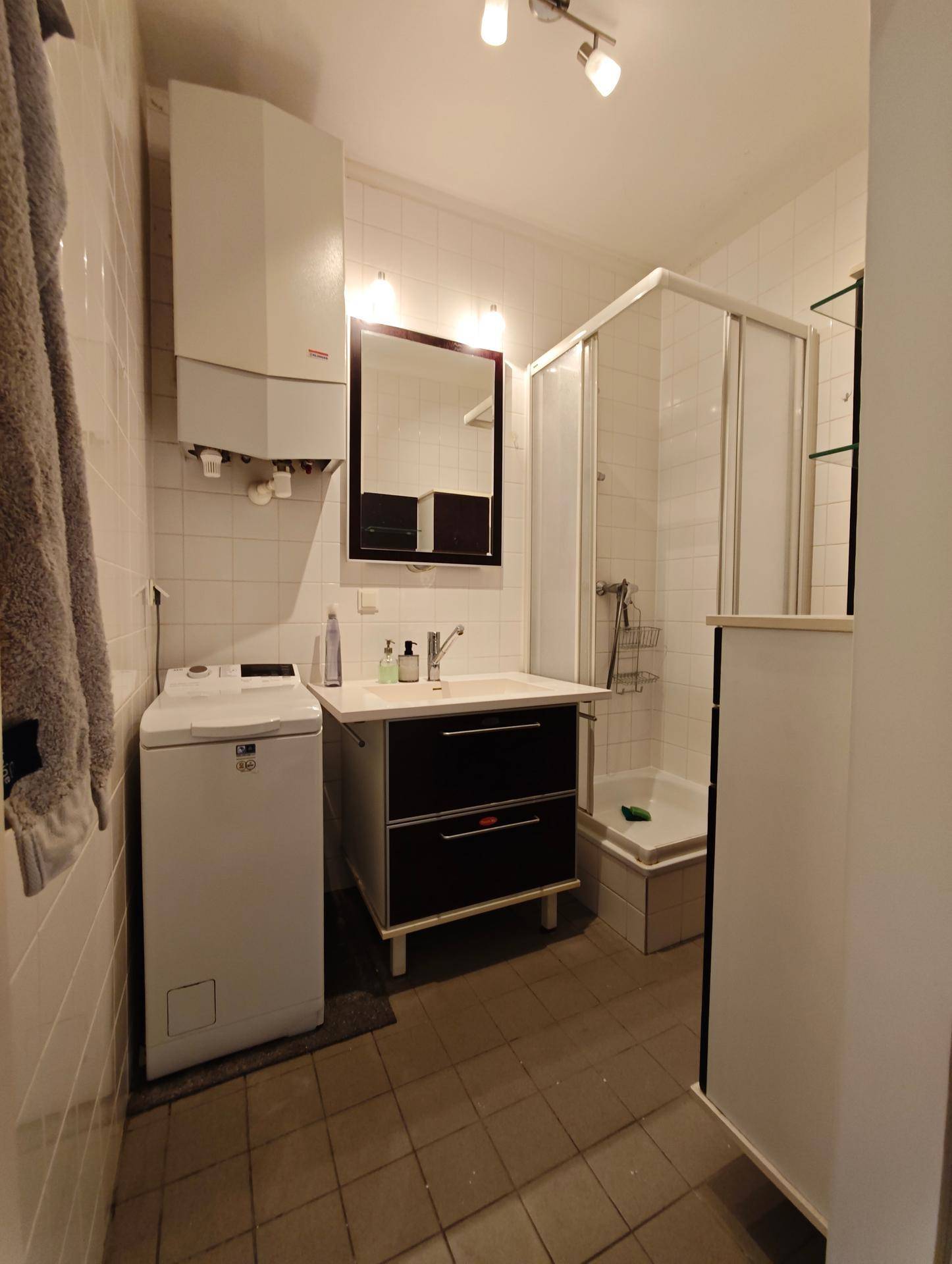 Funktionales Badezimmer mit Dusche, Waschbecken, Waschmaschine und Wandheizung.