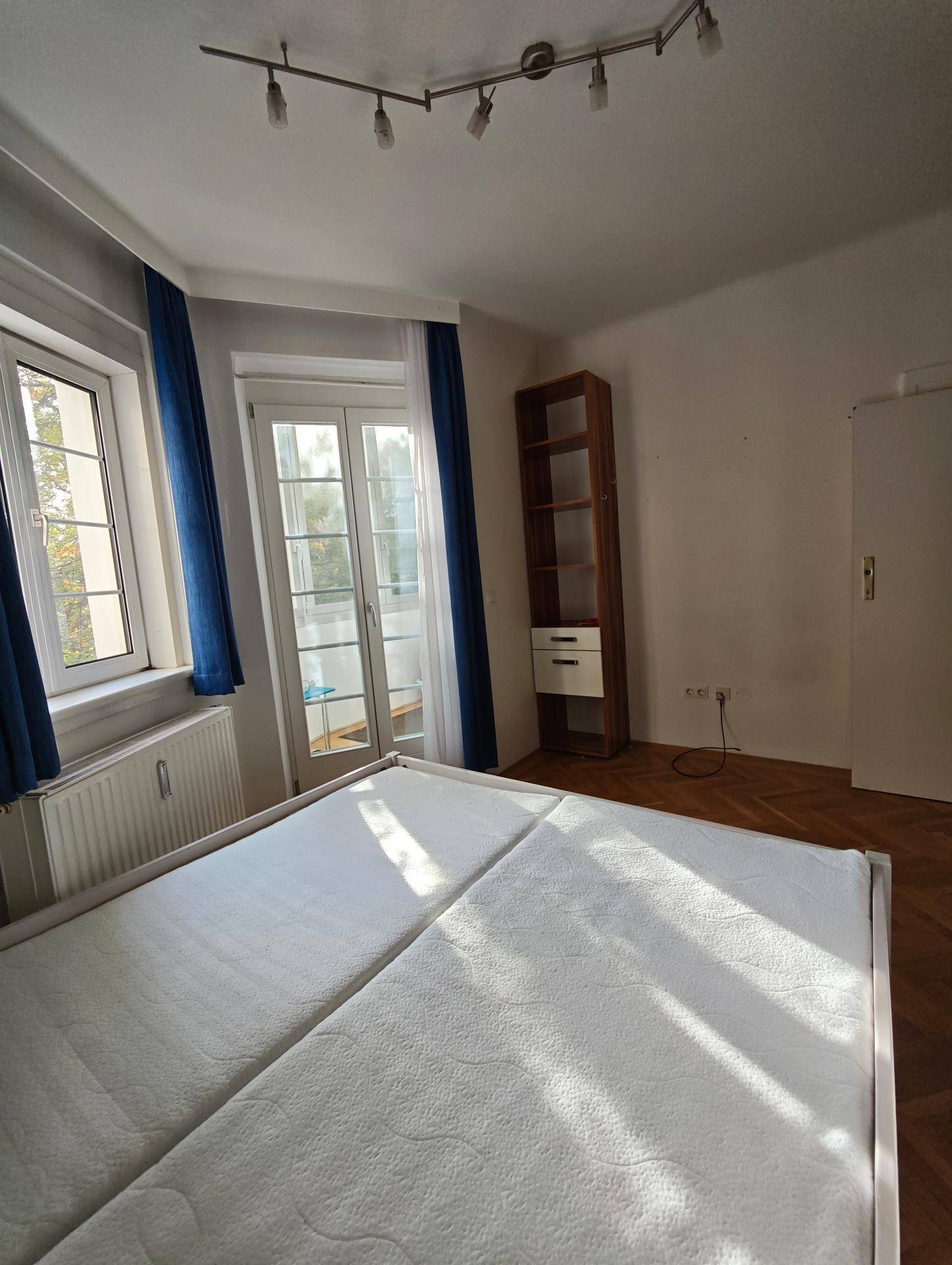 Helles Schlafzimmer mit Parkettboden, Bücherregal und Zugang zu einem französischen Balkon.