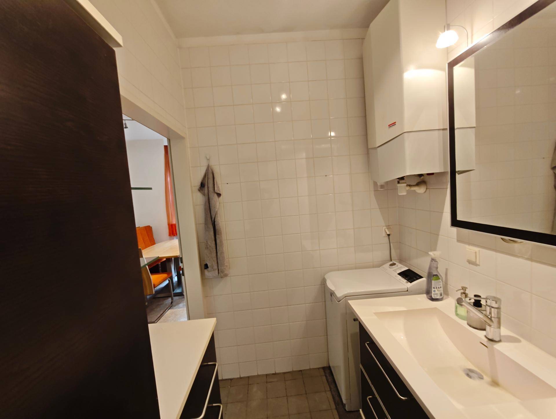 Badezimmer mit Waschmaschine, Waschbecken und weißen Fliesen, gut beleuchtet.