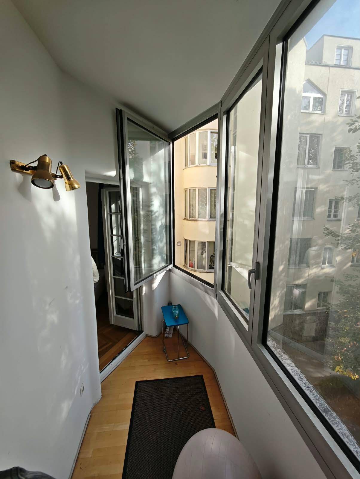 Helle Loggia mit Blick auf die umliegenden Gebäude und Bäume, mit Holzboden.