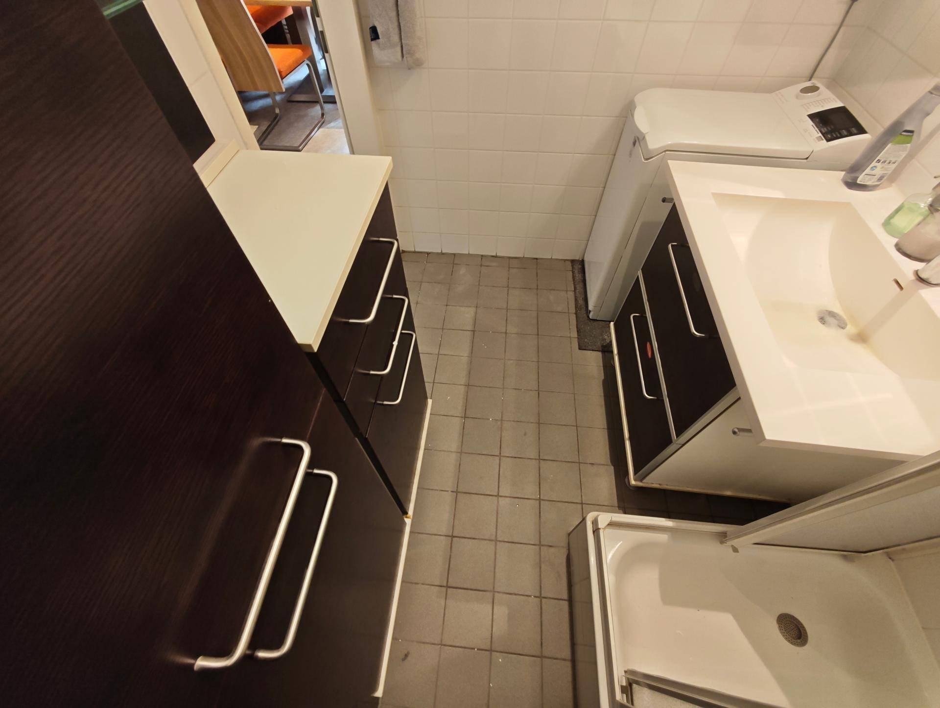 Detailansicht des Badezimmers mit Fliesenboden, Waschmaschine und Unterschränken.