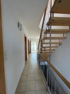 Heller Flur mit Fliesenboden und offener Holztreppe mit Metallgeländer.