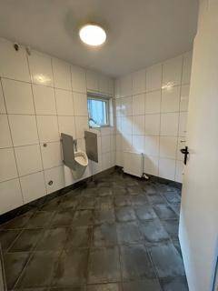 Gefliestes WC mit Urinal, Fenster und Heizkörper, ideal für gewerbliche Nutzung.