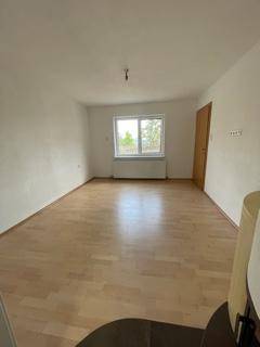 Helles Wohnzimmer mit Parkettboden, großem Fenster und Blick ins Grüne.