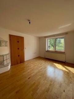 Heller Raum mit Holzdielenboden, Fenster und einem charmanten Kachelofen.