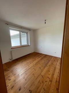 Leerer Raum mit Holzdielenboden und großem Fenster, das viel Tageslicht hereinlässt.