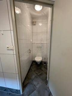 Schlichtes WC mit weißen Fliesen, wandhängendem WC und dunklem Fliesenboden.