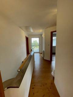 Heller Flur im Obergeschoss mit Holzboden und Zugang zu weiteren Räumen und einem Balkon.