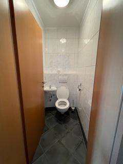 Kleines Gäste-WC mit dunklen Fliesen, wandhängendem WC und kleinem Waschbecken.