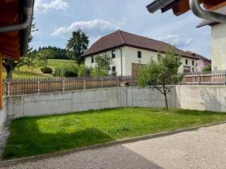 Kleiner Gartenbereich mit Rasenfläche, Betonmauer und Blick auf ein weiteres Gebäude.