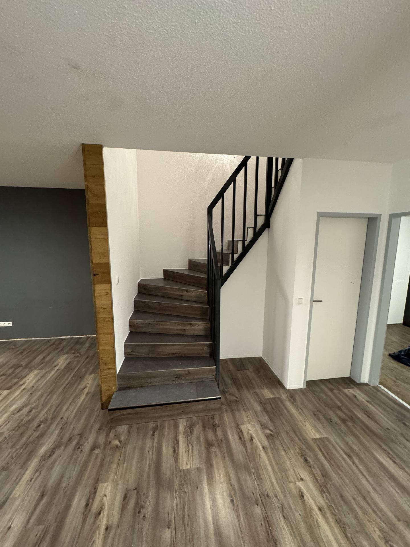 Treppenhaus mit Holzstufen und schwarzem Geländer, das die Etagen miteinander verbindet und gut beleuchtet ist.
