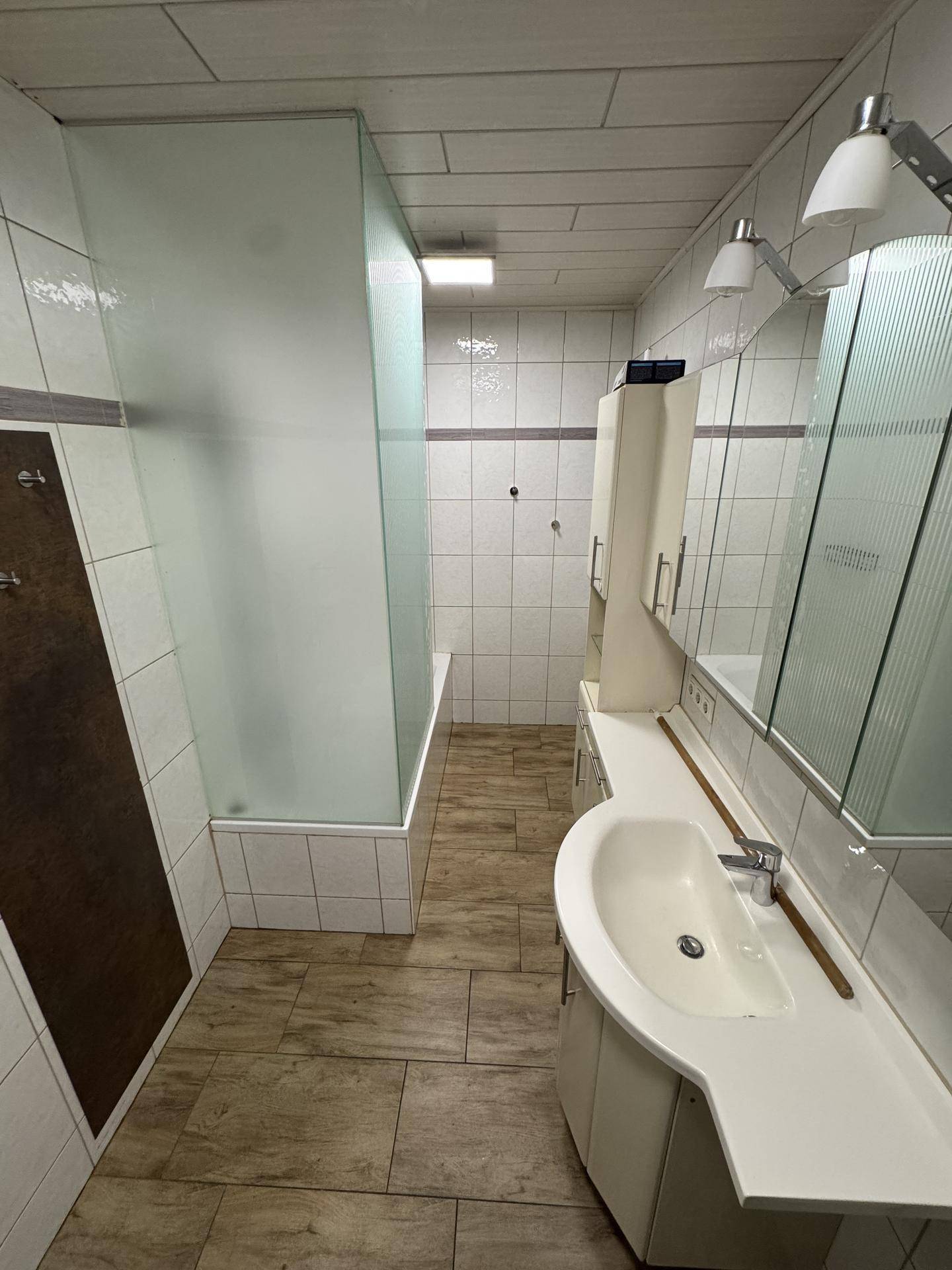 Badezimmer mit Waschtisch, Spiegel und Duschbadewanne, alles in hellen Fliesen gehalten.