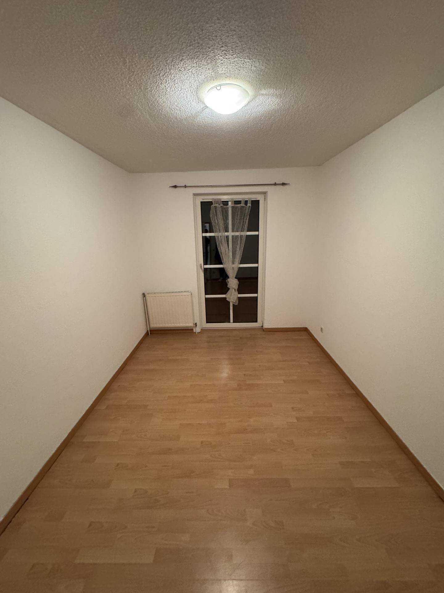 Helles Schlafzimmer mit Holzboden und Zugang zu einem Balkon oder einer Terrasse durch eine Tür.