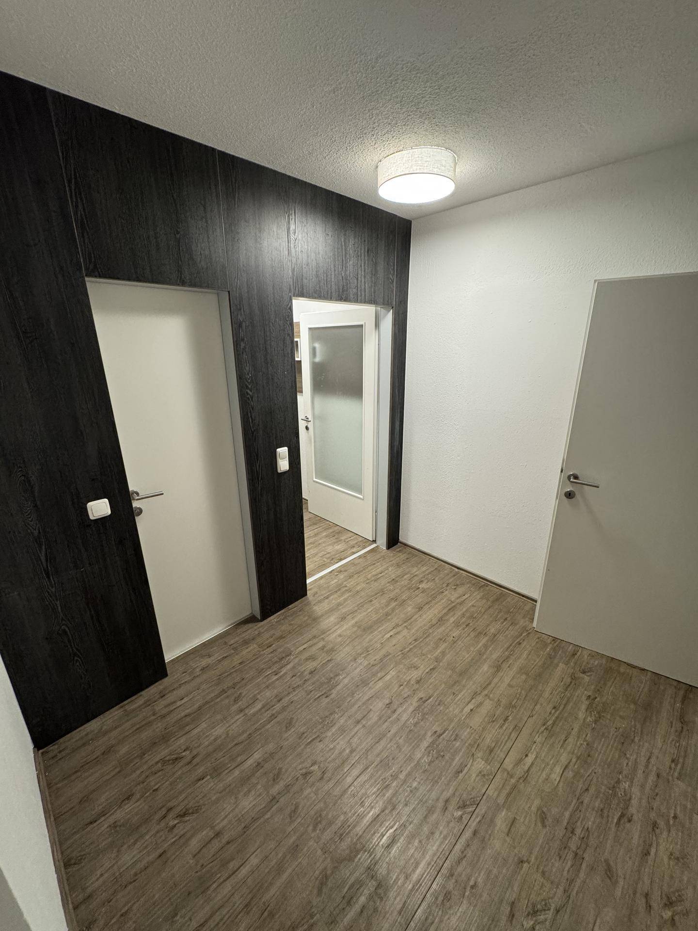 Geräumiger Flur mit dunkler Holzverkleidung und Laminatboden, der zu verschiedenen Zimmern führt.