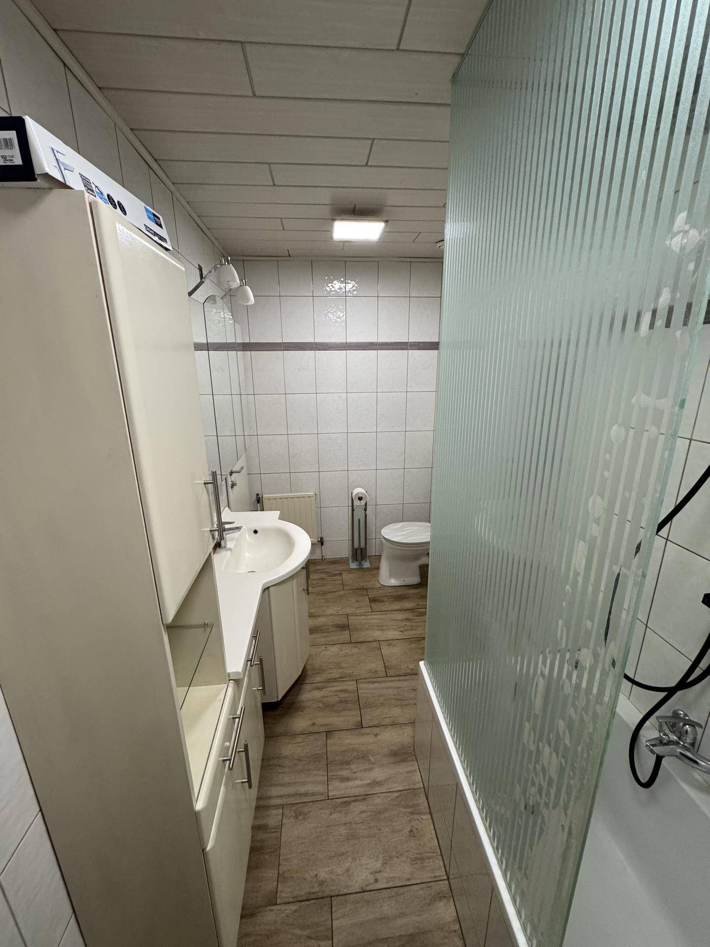 Modernes Badezimmer mit Fliesenboden, Waschtisch und Duschbadewanne hinter einer Glaswand.