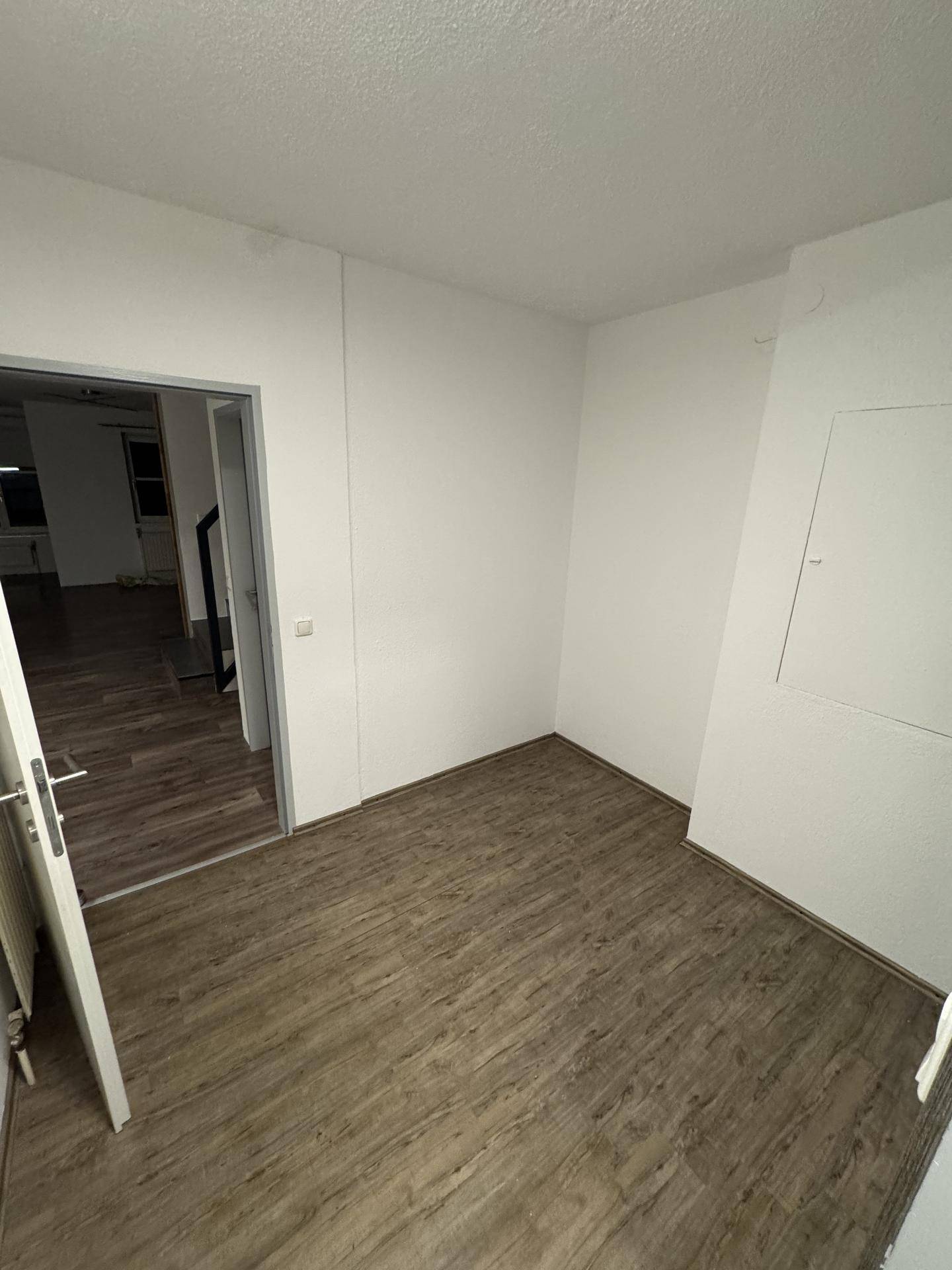 Leerer Raum mit Laminatboden und weißen Wänden, bereit zur individuellen Gestaltung und Nutzung.
