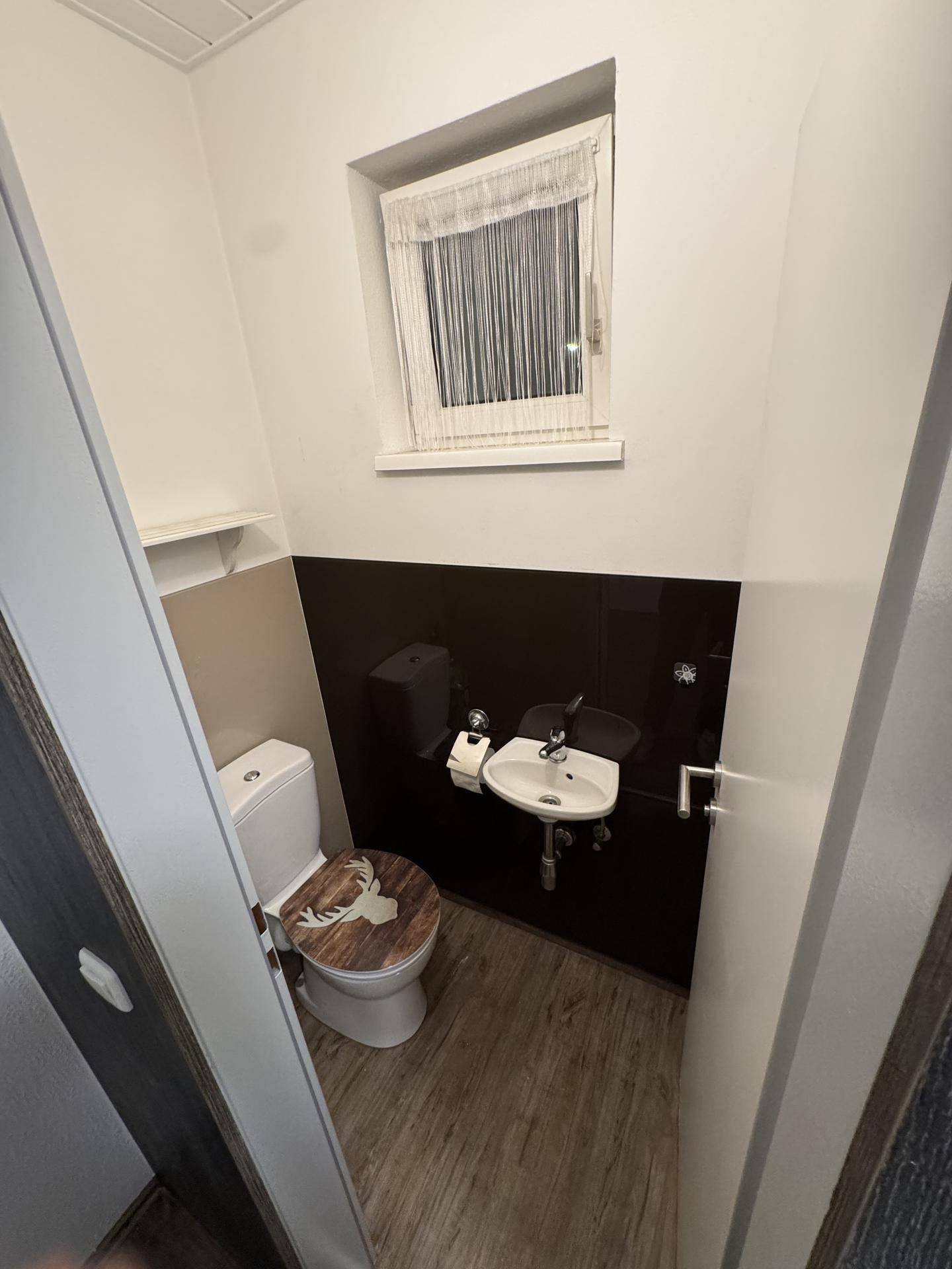 Kleines Gäste-WC mit Fenster, dunklen Fliesen und einem Waschbecken, ausgestattet mit Hirschmotiv.