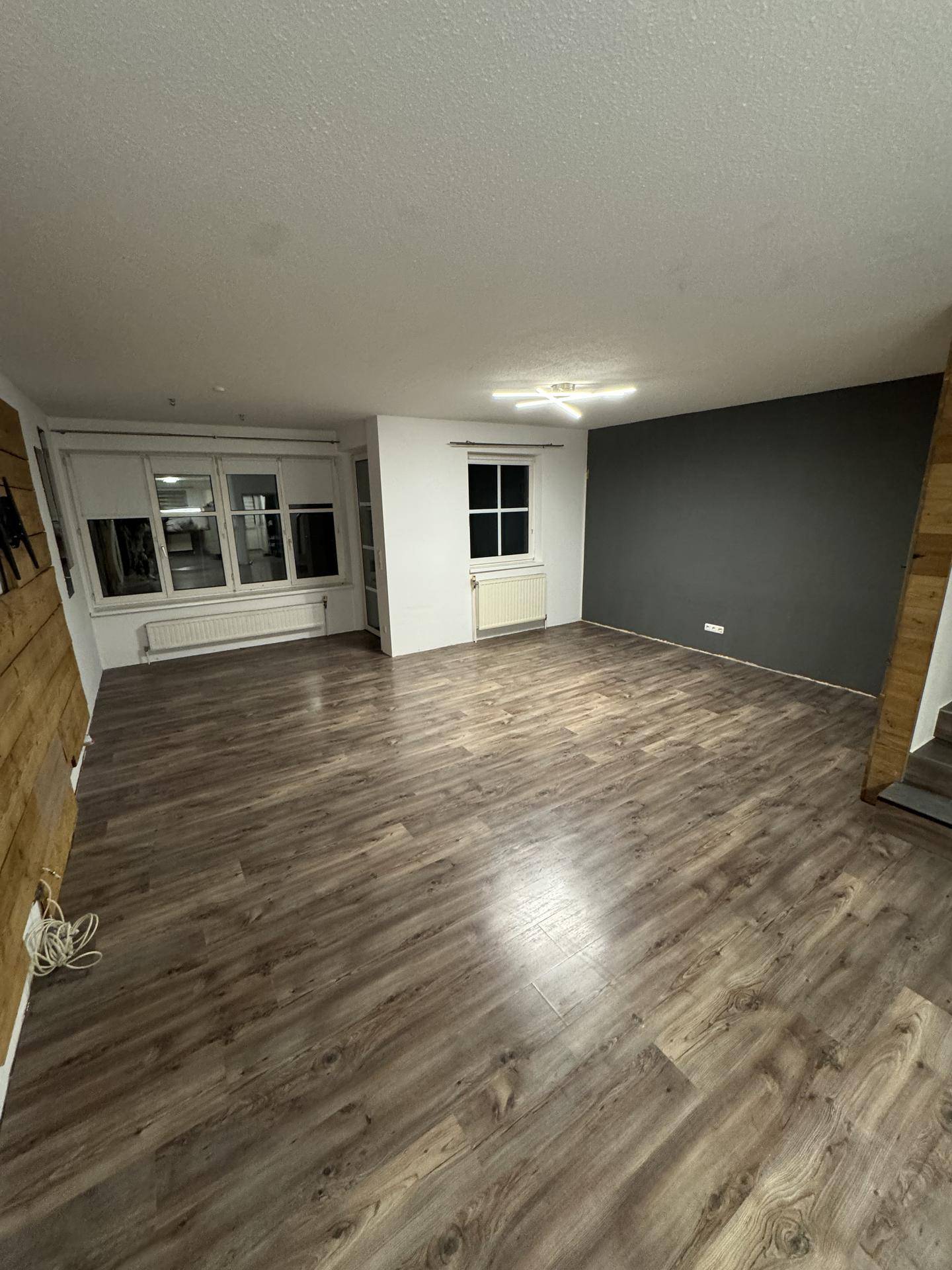 Geräumiges Wohnzimmer mit Laminatboden, großen Fenstern und einer dunklen Akzentwand für Unterhaltung.