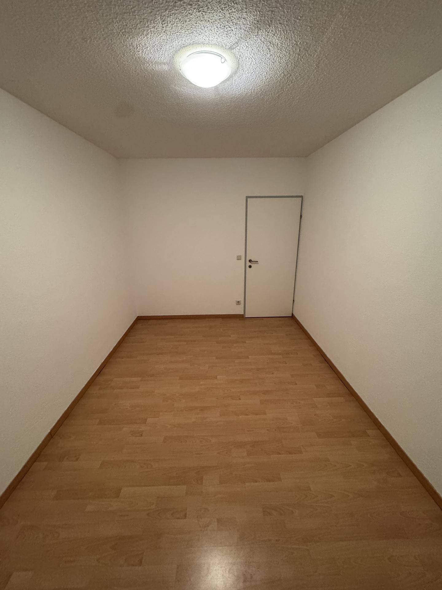 Leeres Schlafzimmer mit Laminatboden und weiß gestrichenen Wänden, bereit zur individuellen Einrichtung.