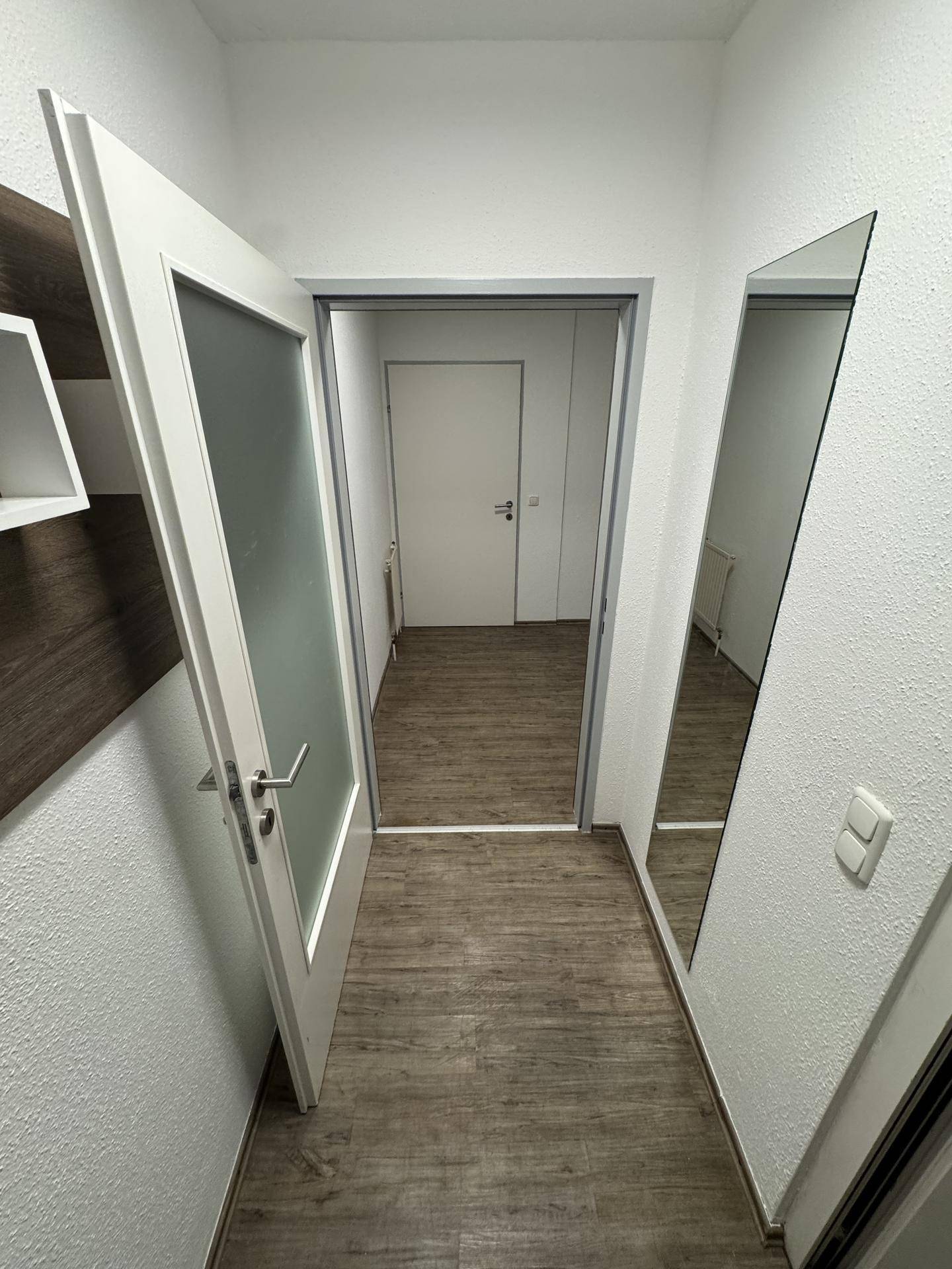 Heller Flur mit Laminatboden und weiß gestrichenen Wänden, der zu weiteren Räumen führt.