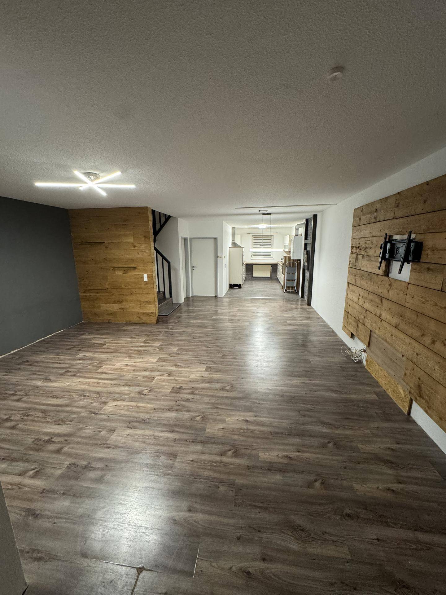 Großer offener Wohnbereich mit Laminatboden und Holzwandverkleidung, ideal für Geselligkeit und Entspannung.