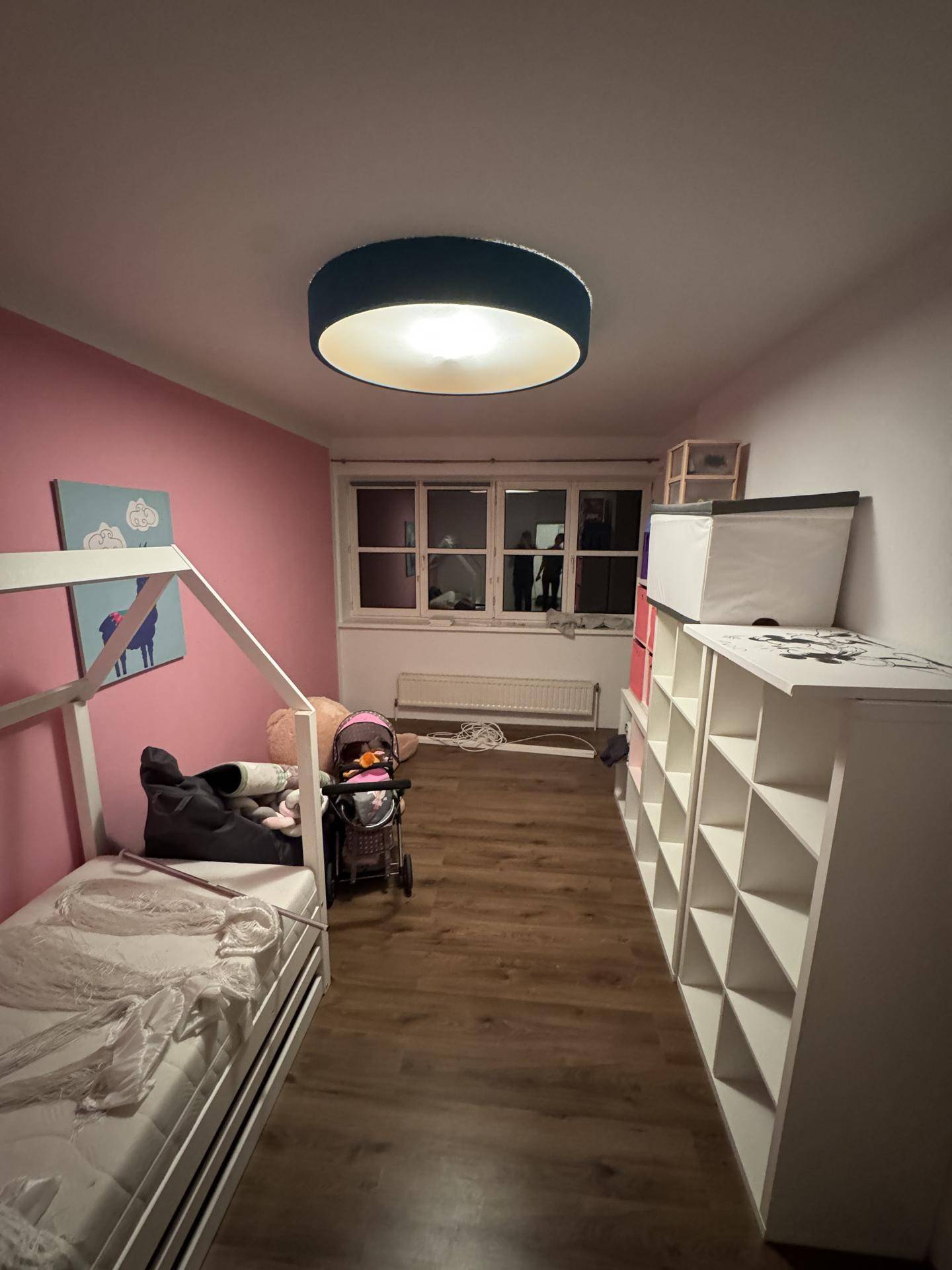 Kinderzimmer mit rosa Akzentwand, Laminatboden und einem Kinderbett, hell und freundlich gestaltet.