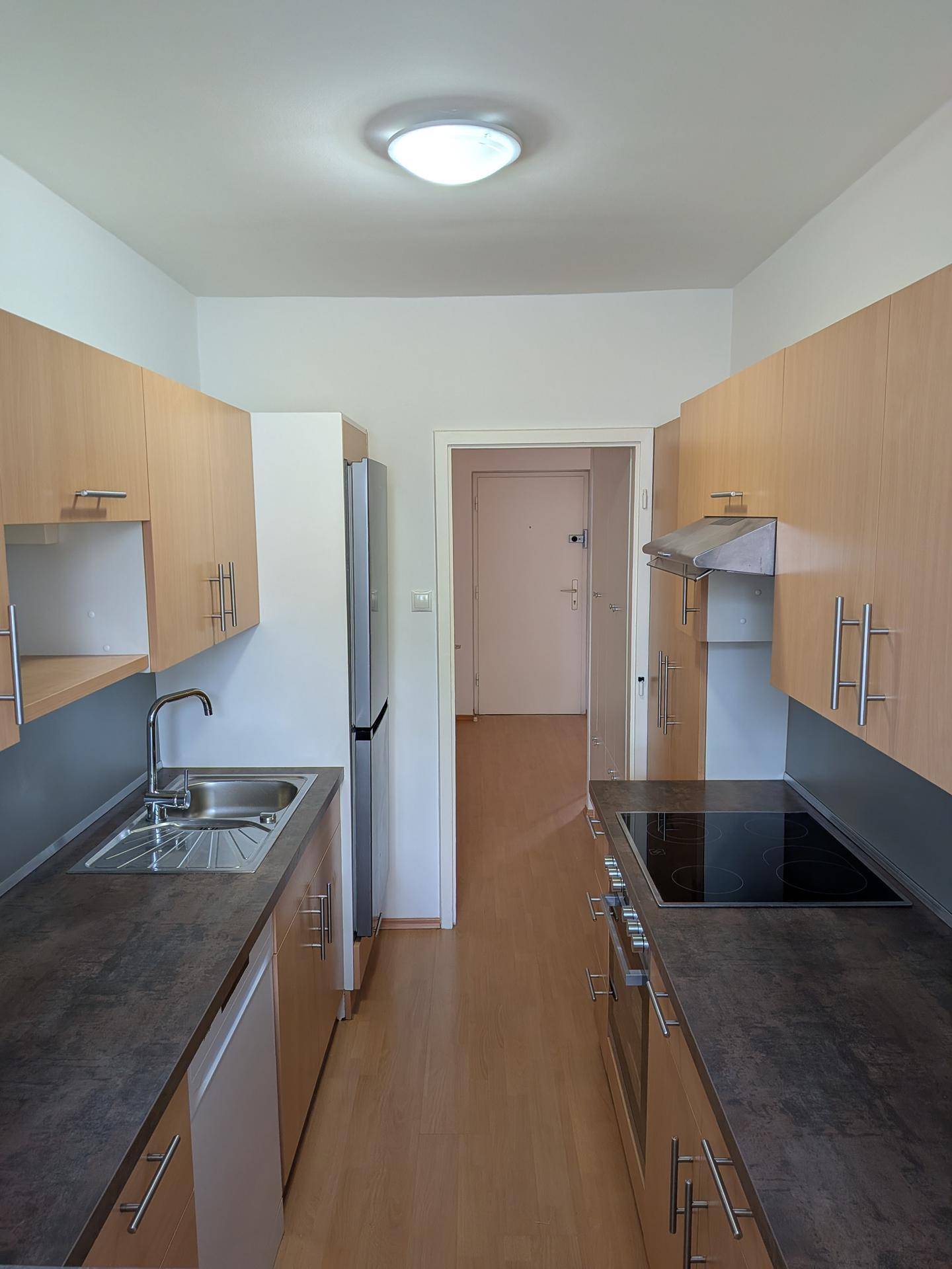 Funktionale Küche mit hellen Holzschränken, dunklen Arbeitsplatten und modernen Geräten.