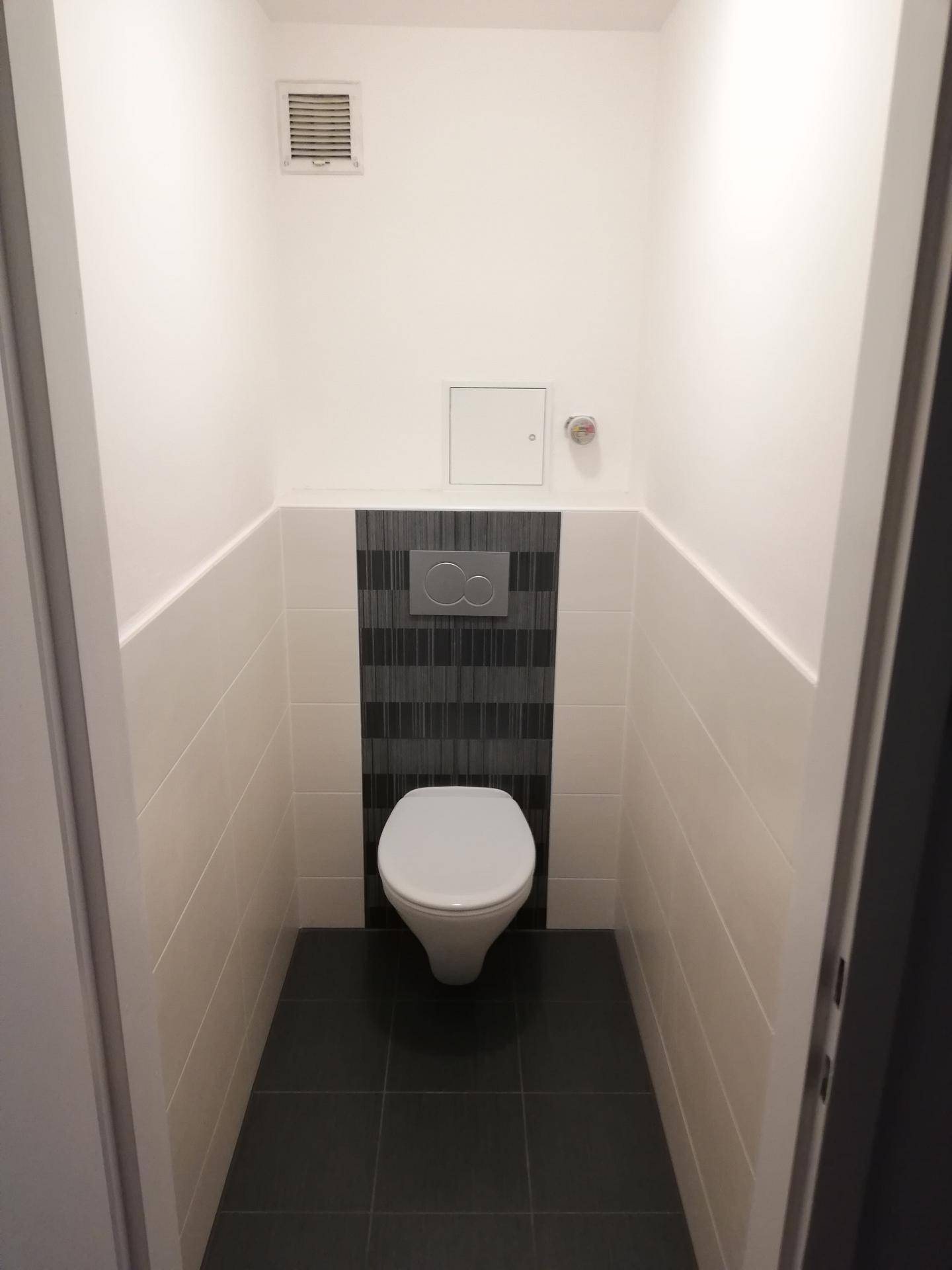 Separates WC mit wandhängender Toilette und modernen Fliesen in Weiß und Grau.