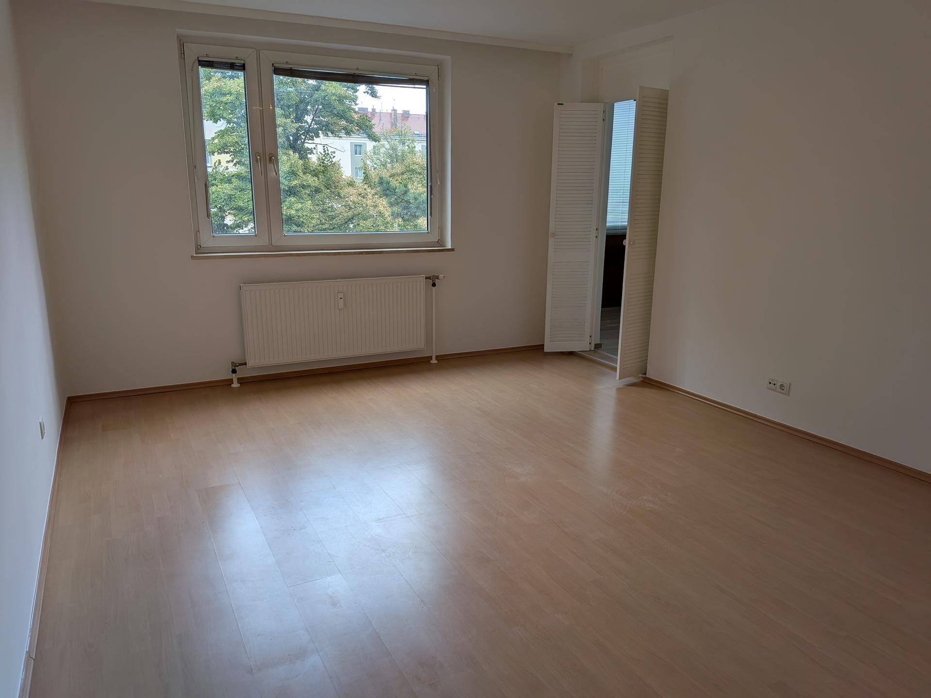 Geräumiges Schlafzimmer mit großem Fenster, Blick ins Grüne und hellem Laminatboden.