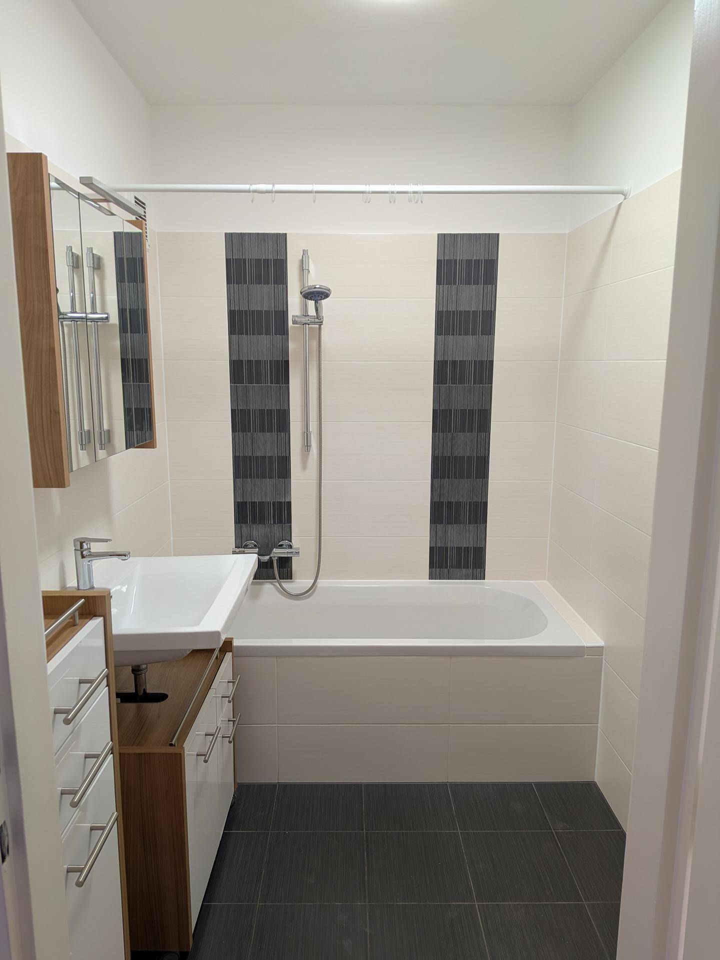 Modernes Badezimmer mit Badewanne, Dusche, Waschbecken und Spiegelschrank in hellen und dunklen Fliesen.