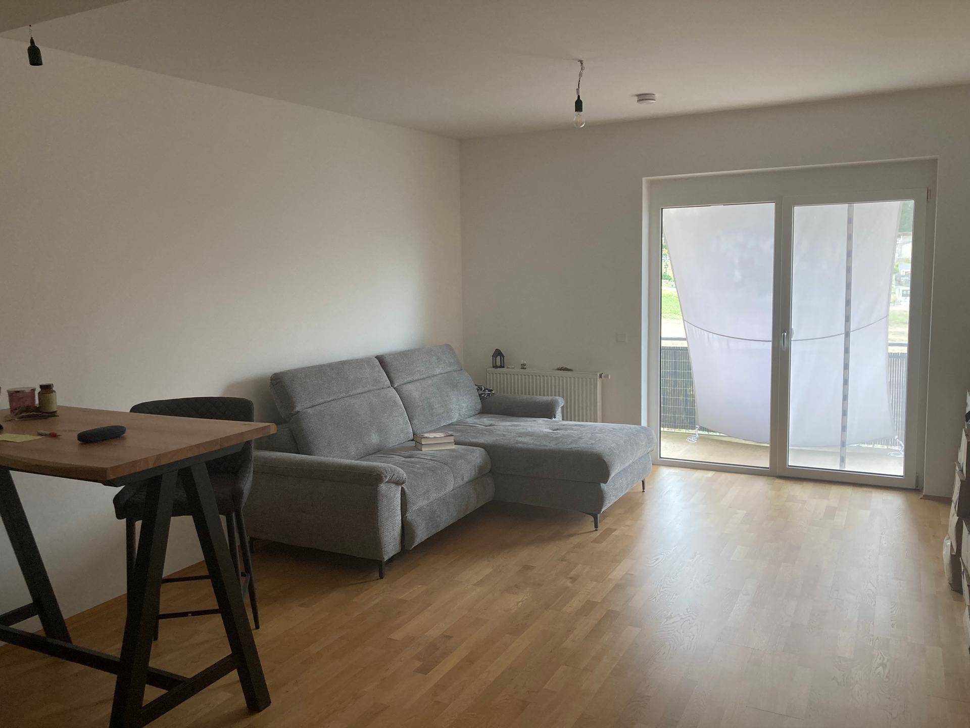 Helles Wohnzimmer mit modernem grauen Sofa, Holzboden und Zugang zum Balkon.
