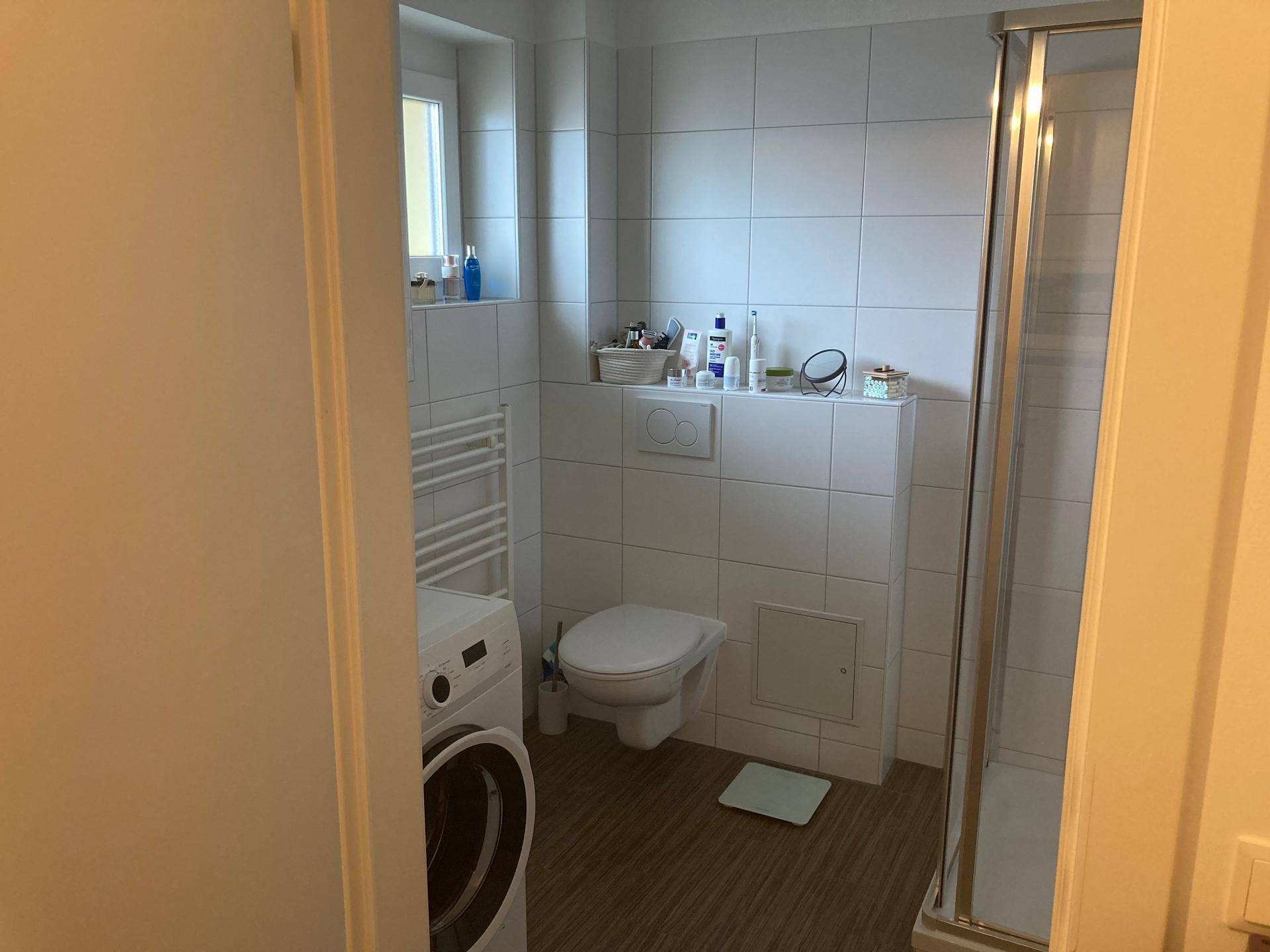 Modernes Badezimmer mit Dusche, wandhängendem WC, Waschmaschine und Handtuchheizkörper.
