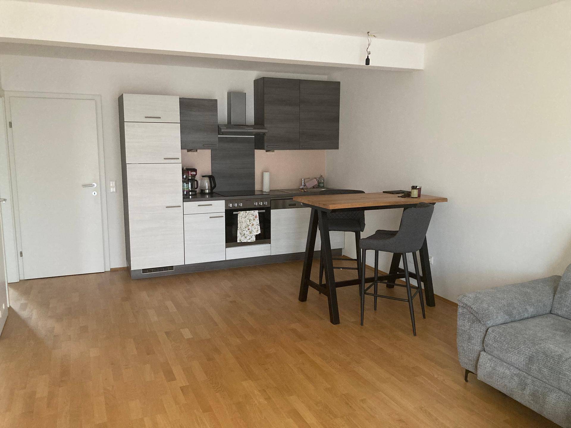Offene Küche mit modernen grauen Schränken, integriertem Essbereich und Holzboden.