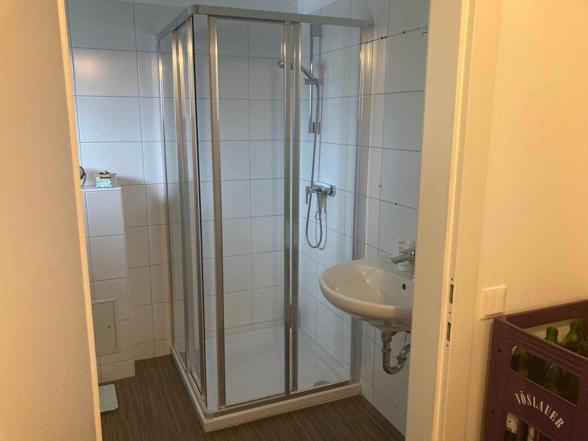 Badezimmer mit Duschkabine, Waschbecken und weißen Wandfliesen, funktional und hell.